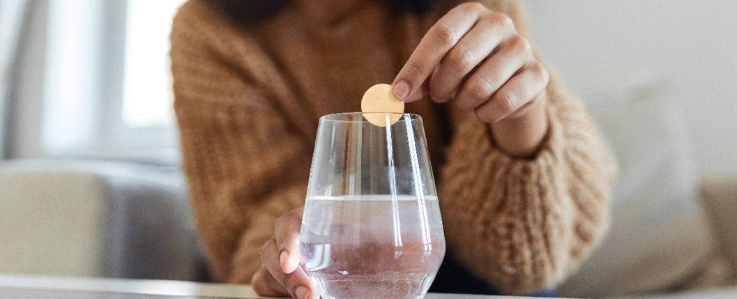 mulher colocando uma cápsula de remédio em um copo com água 
