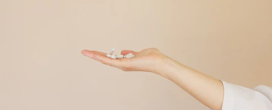 mão do lado segurando algumas pílulas brancas de remédio com um fundo rosa atrás
